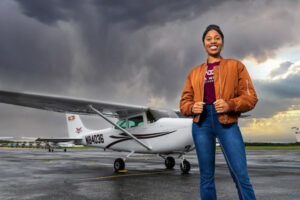 A young woman stands in front of a small plane