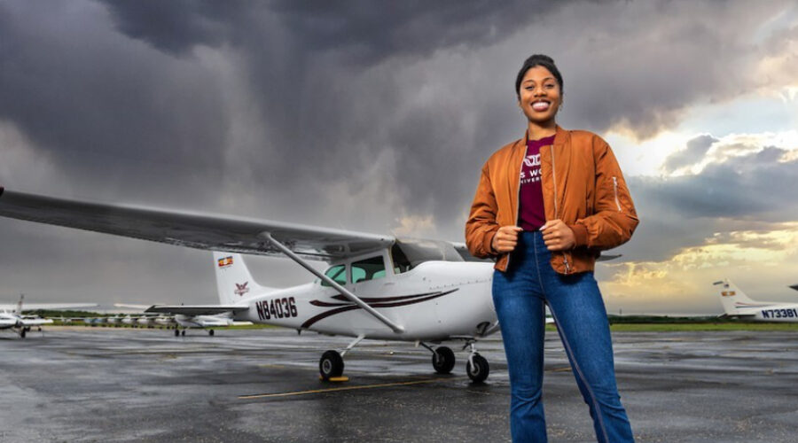 A young woman stands in front of a small plane